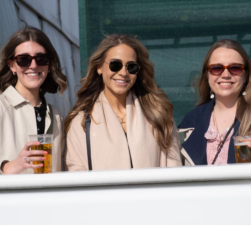Three young race goers in coats pose at Hereford