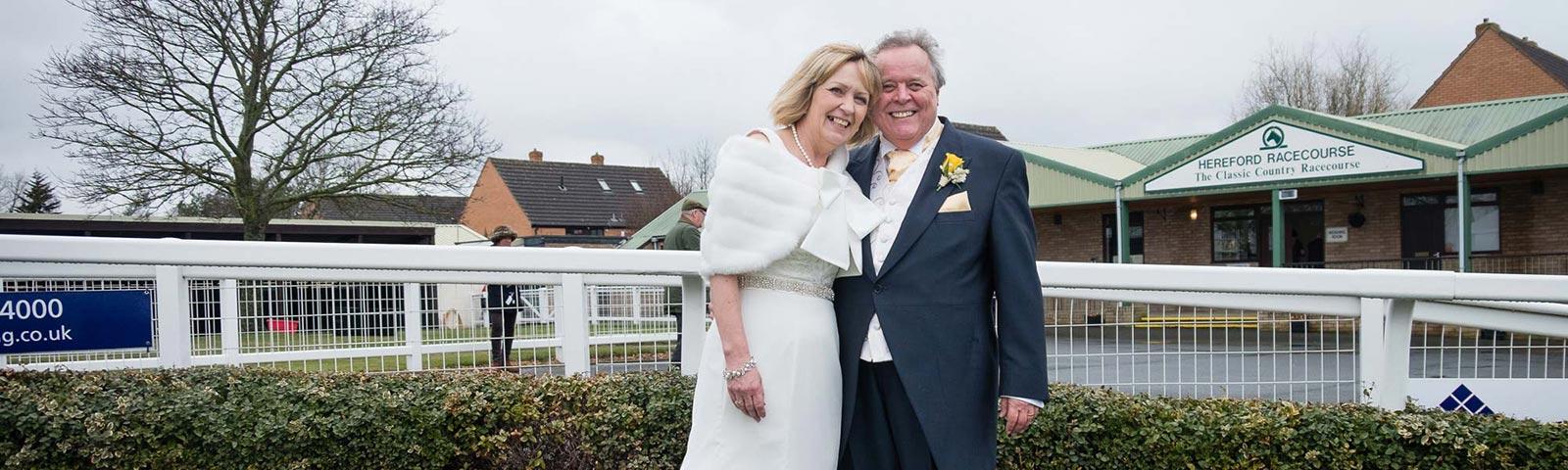 Newlyweds standing in front of the Hereford Racecourse entrance.