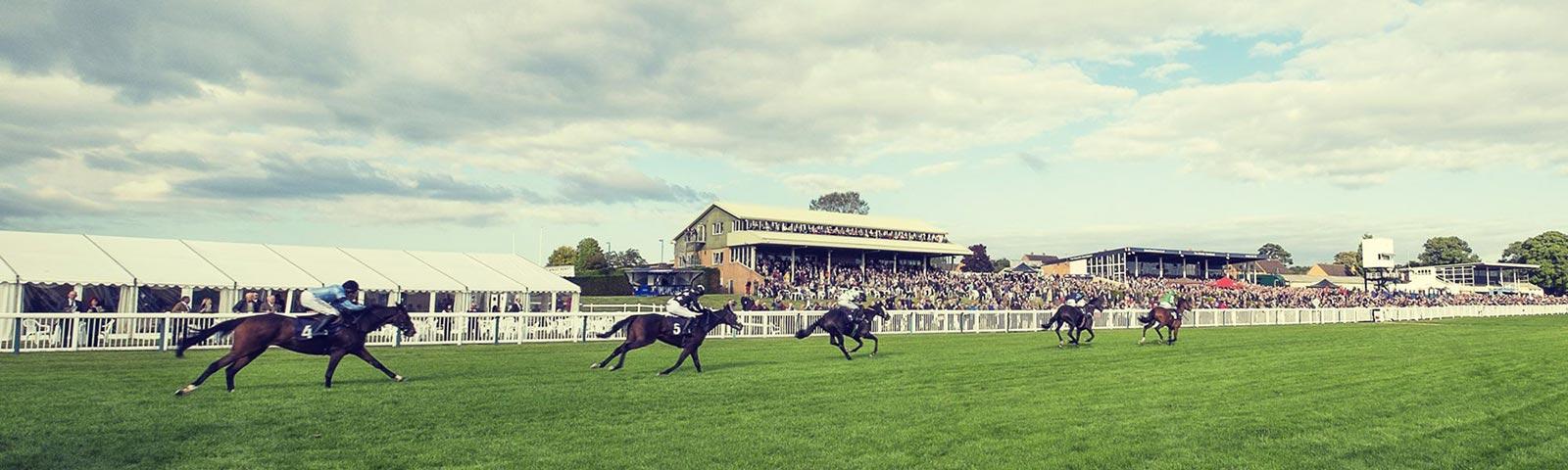 Jockeys racing at Hereford with crowds in the background.